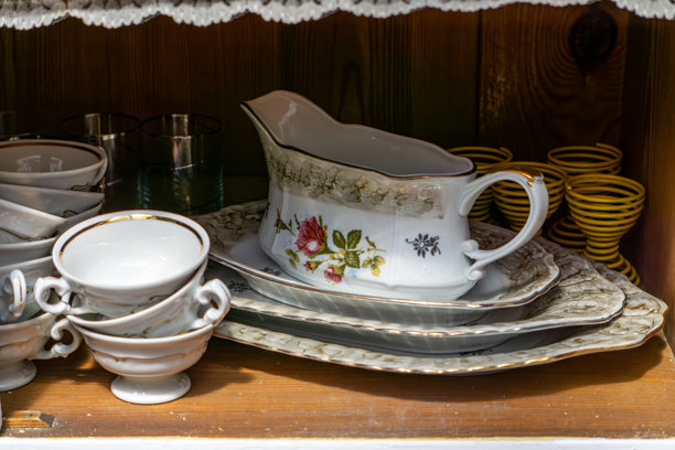 一套瓷杯、花卉酱汁壶和装饰盘子整齐地摆放在木制架子上。复古风格，温馨的乡村厨房氛围，传统的餐具带有手绘细节。图片下载