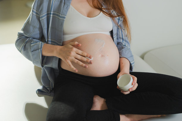 怀孕母亲。孕妇在大肚子上涂抹护肤霜，呵护自己的肌肤。预防妊娠纹的化妆品。女孩在家享受怀孕时光。母婴健康概念。图片下载