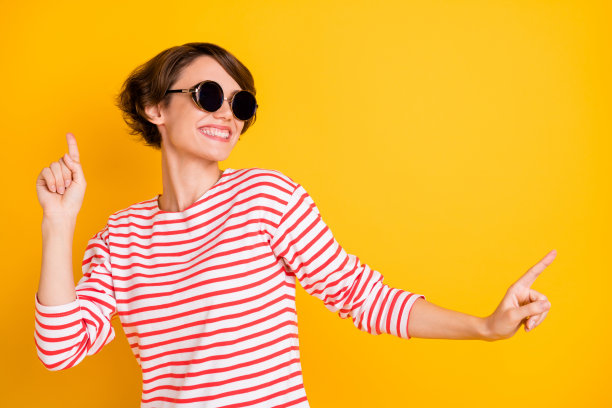 年轻迷人、可爱、微笑、快乐、积极的女孩戴着太阳镜在黄色背景上跳舞的照片图片下载