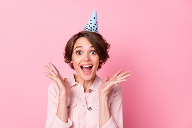 兴奋的女孩佩戴生日帽的照片肖像，背景为柔和的粉色。图片下载