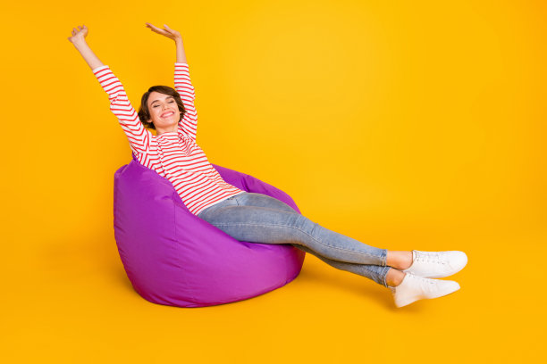 全身照片：年轻迷人、可爱、微笑、积极的女孩在黄色背景下的扶手椅上睡觉并伸展身体。图片下载