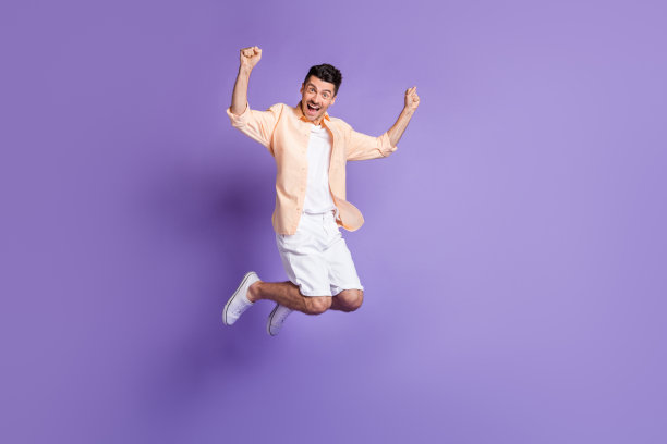 全身照片，欢呼的棕发男孩穿着桃色衬衫、短裤和运动鞋，背景为淡紫色。图片下载