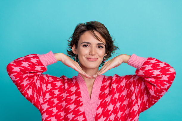 年轻女士的照片肖像，双手托着脸，穿着时尚的红色服装，背景为水绿色。图片下载