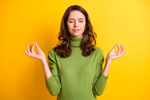 年轻美丽、平静快乐、微笑心情愉悦的女性在黄色背景下闭眼做瑜伽的照片图片下载