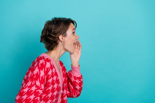 年轻女士的照片肖像，侧面分享秘密，空白空间，穿着时尚的红色服装，背景为水绿色。图片下载