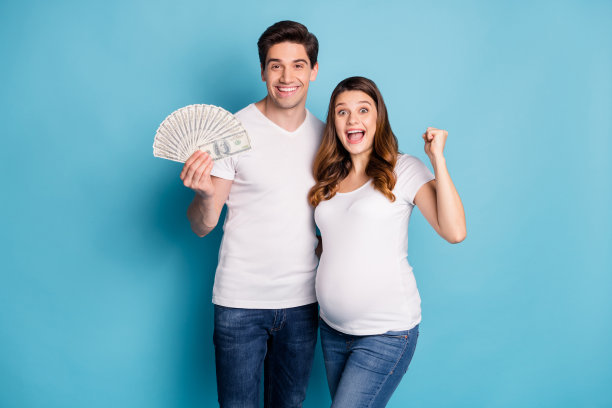 欢呼的孕妇情侣穿着白色T恤和牛仔裤，展示着钱，背景为青色。图片下载