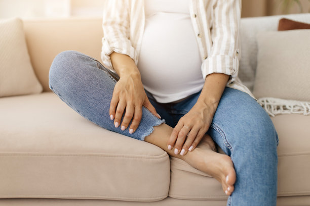孕妇坐在家里的沙发上按摩脚踝的特写镜头图片下载
