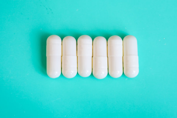 一排白色胶囊在明亮的青绿色背景上居中排列。这张极简风格的照片强调了医疗和制药领域的纯净与精确。图片下载