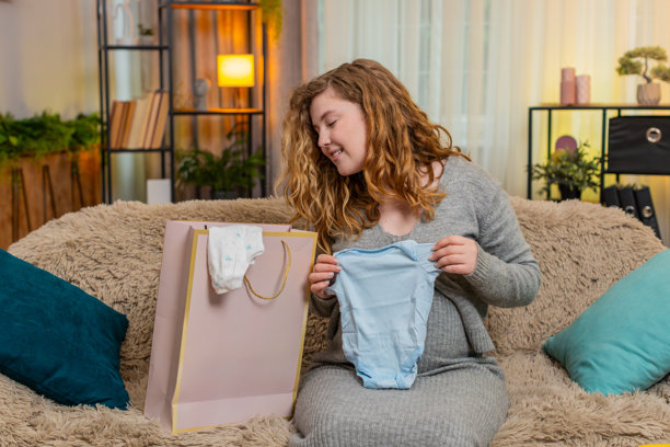 孕妇正在拆包购物袋里的婴儿衣物，对新购买的物品感到兴奋和满意图片下载