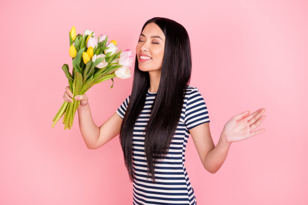 亚洲女孩在粉色背景下，闭着眼睛微笑，陶醉于花香中，满脸喜悦的照片肖像。图片下载