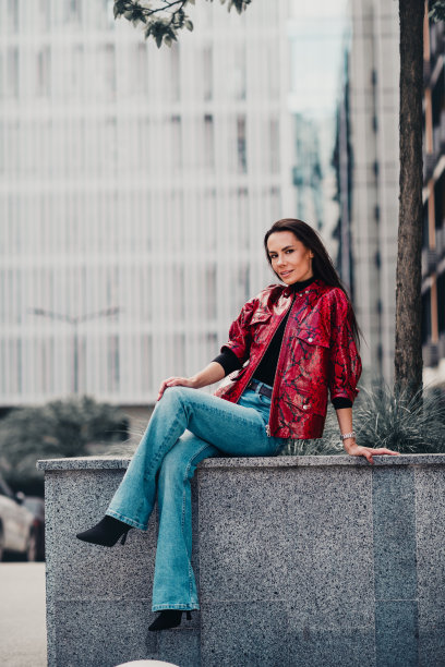 时尚女性在城市环境中穿着红色印花夹克和牛仔裤，享受户外城市氛围，竖版照片图片下载