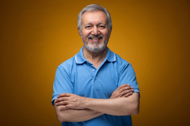 穿着蓝色T恤的老年帅气男士肖像照片，背景为黄色。图片下载