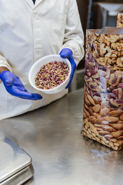 工人手持一碗干燥的开心果，旁边有一个袋子，竖版照片，留有空白区域。图片下载