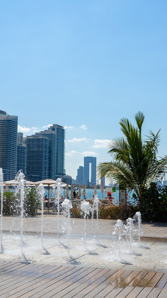 棕榈岛西海滩的木栈道，阳光明媚的夏日，棕榈树和喷泉映衬着波斯湾海岸的摩天大楼。漫步城市。竖版图片图片下载