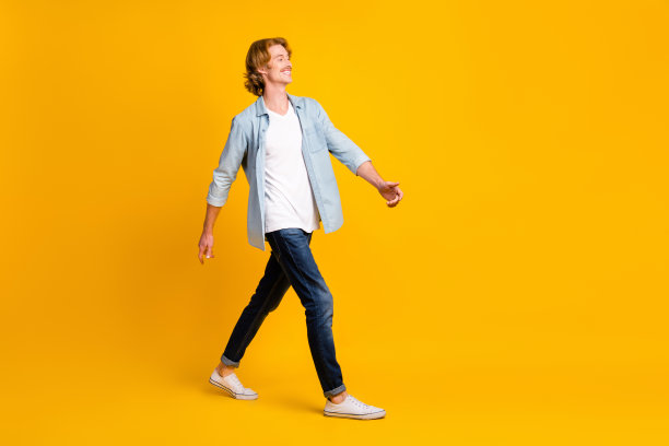 乐观男士的全身侧面照片，穿着衬衫、牛仔裤和运动鞋，背景为黄色。图片下载
