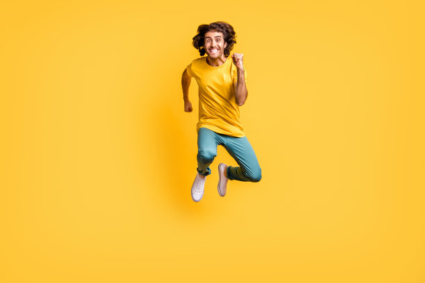 年轻帅气的疯狂兴奋快乐微笑男子在黄色背景上快速跳跃奔跑的全身照片图片下载