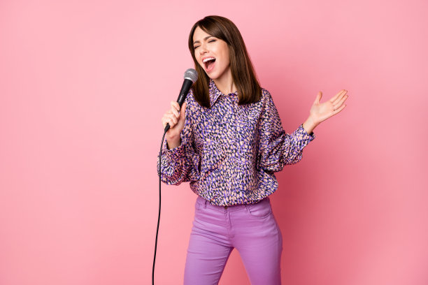 女性在粉色背景下唱歌，手持麦克风的肖像照片图片下载