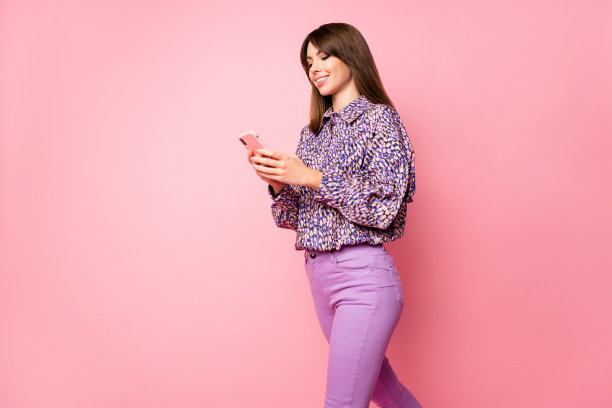 女性双手握着手机走路的照片肖像，背景为柔和的粉色。图片下载