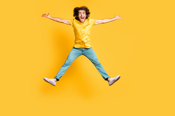 年轻帅气、微笑、兴奋、疯狂的男人在黄色背景上跳跃庆祝胜利的全身照片图片下载