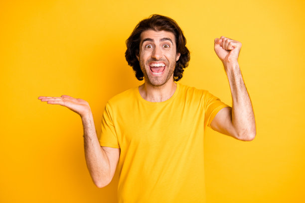 快乐男人的照片肖像，庆祝时举起拳头，手中握着空白空间，背景为明亮的黄色。图片下载