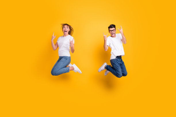 穿着T恤的时尚有趣的人们在黄色背景下高高跳起，做出摇滚手势的全身照片图片下载