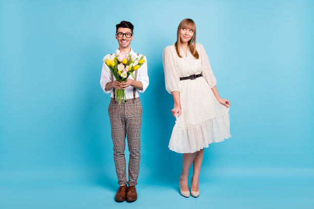 害羞迷人的年轻情侣穿着白色服装，手持花束在蓝色背景下约会的照片图片下载