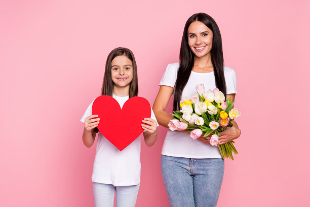 母亲和小女儿在春天的粉色背景下，手捧一束红色心形郁金香的照片肖像图片下载