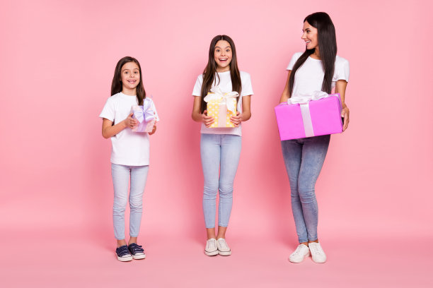 乐观的三位女性母女穿着白色衣服，手持礼物，背景为粉色，完整照片。图片下载