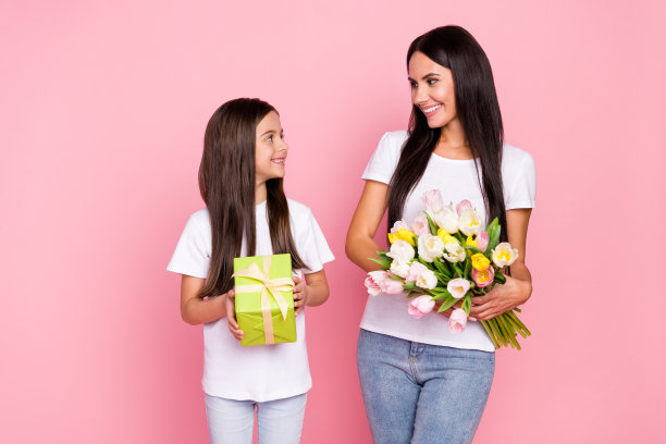 母亲和小女儿手捧礼物盒和郁金香花束的照片肖像，背景为柔和的粉色。图片下载