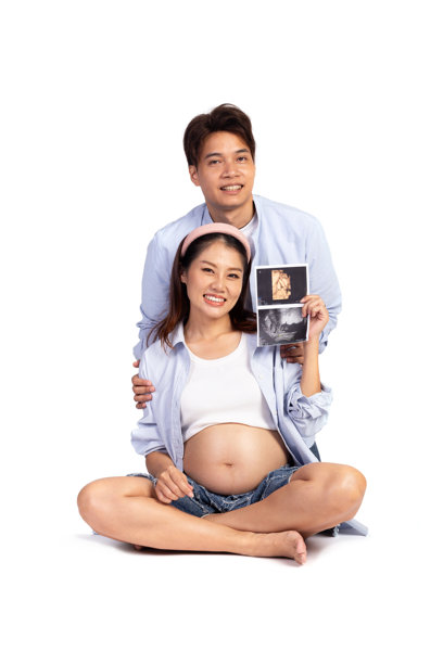 快乐的亚洲家庭夫妇在白色背景下独处，丈夫和怀孕的妻子坐在一起。美丽的孕妈妈怀抱着超声波婴儿照片，坐在新爸爸身旁。图片下载