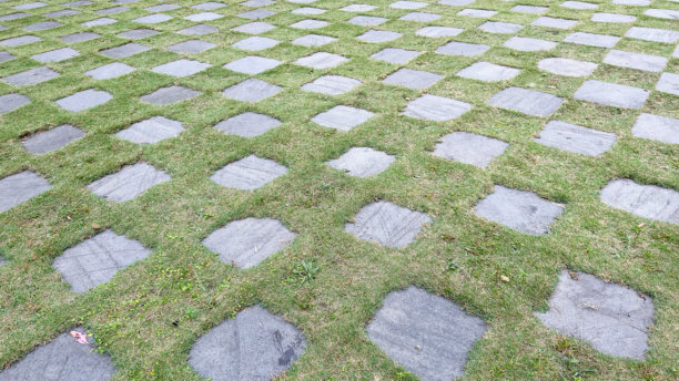 这张图片展示了一种网格图案的浅灰色方形石板，镶嵌在生机勃勃的绿色草坪中，形成了一个既美观又实用的户外小径或地面覆盖。图片下载