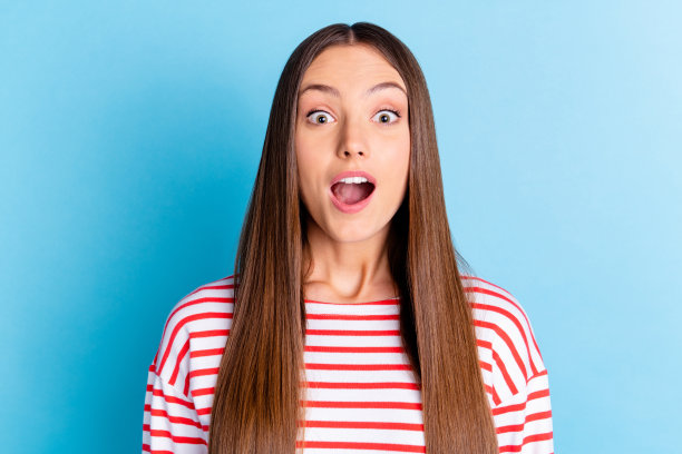 穿着条纹服装、眼睛大睁、嘴巴张开的搞笑惊讶年轻女士的照片，背景为蓝色。图片下载