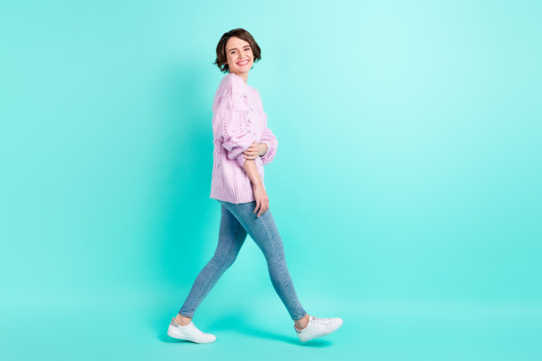 穿着紫色毛衣的甜美可爱年轻女士在青色背景下独自走路的全身照片图片下载