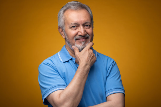 穿着蓝色T恤的老年帅气男性肖像照片，背景为黄色。图片下载