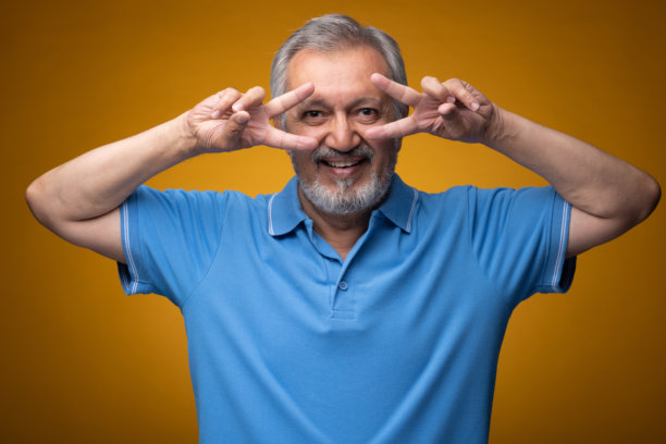 穿着蓝色T恤的老年帅气男性肖像照片，背景为黄色。图片下载