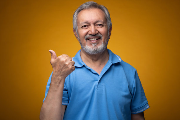 穿着蓝色T恤的老年帅气男性肖像照片，背景为黄色。图片下载