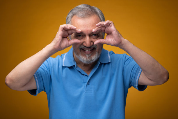 穿着蓝色T恤的老年帅气男性肖像照片，背景为黄色。图片下载