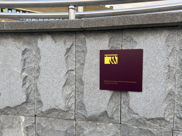 现代警告牌，带有爪子图标，安装在光滑的灰色花岗岩墙上，结合了视觉清晰度与大胆对比，通过简单的图形语言在公共环境中传达安全信息。图片下载