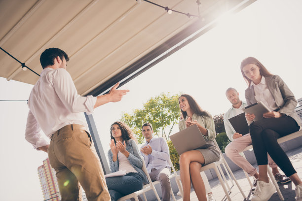 低角度拍摄的照片，展示了一位男性领导者（CEO）与同事们开会，快乐的微笑着，大家在户外鼓掌工作。图片下载