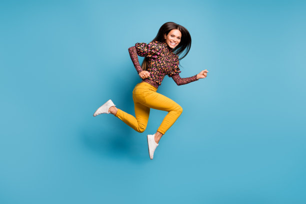 年轻、开朗、迷人的微笑女性在蓝色背景上快速奔跑的侧面全身照片图片下载