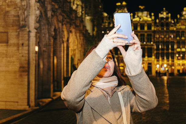 一个女孩在夜晚的城市里用智能手机拍摄建筑照片。图片下载