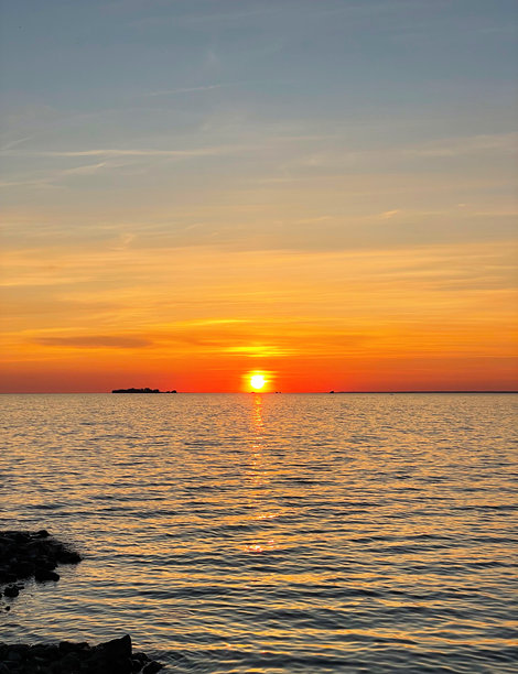 美丽的海上日落。太阳在水面上落下。天空被明亮的色彩装点。水面上的阳光小径。夏季的傍晚。日落海滩。竖版照片。图片下载
