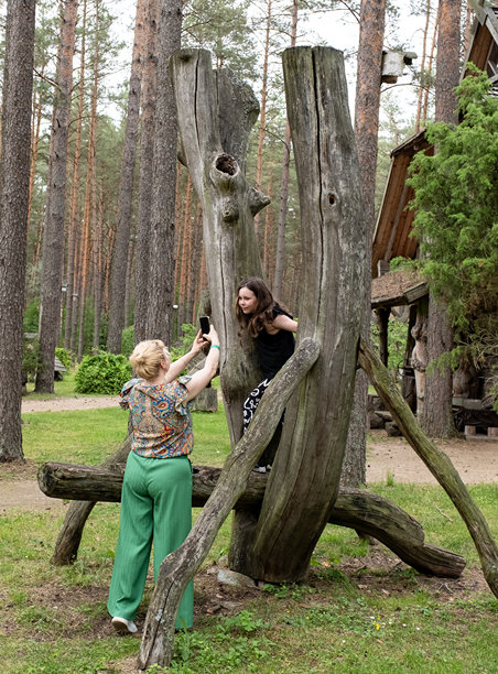 一位年轻的白人女性在树干制成的木秋千背景下，用手机拍摄一名10岁女孩的照片。图片下载