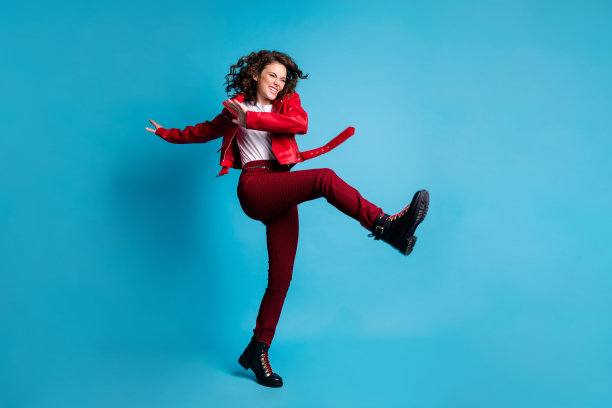 穿着红色夹克、裤子和靴子的乐观女孩在蓝色背景下跳舞的全身照片图片下载