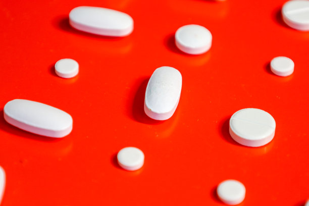 单个和椭圆形的白色药片松散地排列在丰富的红色背景上。这张照片强调了药物制剂的普遍性，象征着现代医学和医疗保健的可及性。图片下载