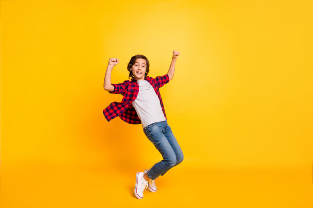 兴奋快乐的学生踮起脚尖，双拳举起，站在黄色背景前的全身侧面照片图片下载