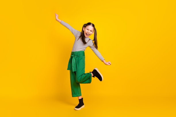 年轻女学生的全身侧面照片，开心地微笑，享受乐趣，背景为黄色。图片下载