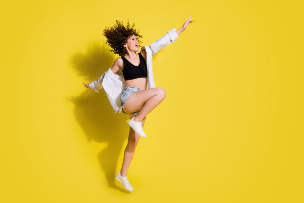 充满活力的女孩穿着短裤和运动鞋在黄色背景上跳跃的全身侧面照片图片下载