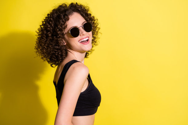 侧面肖像照片，愉快的女性佩戴黑色太阳镜，笑容灿烂，背景色彩鲜艳，留有空白空间。图片下载