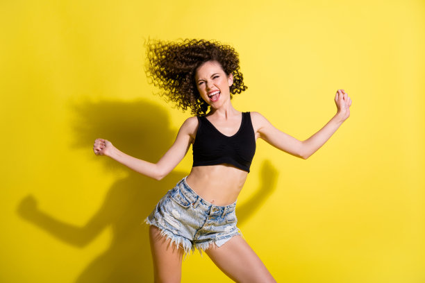 穿着黑色上衣和短裤的乐观波浪发女孩在黄色背景下跳舞的照片图片下载